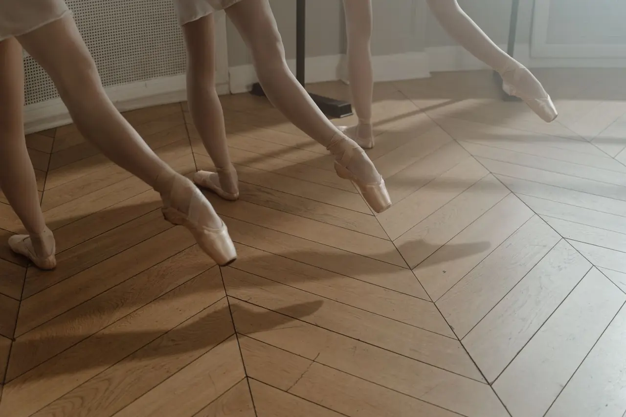 Close-up of ballet dancers practicing pointe work on natural studio wood flooring