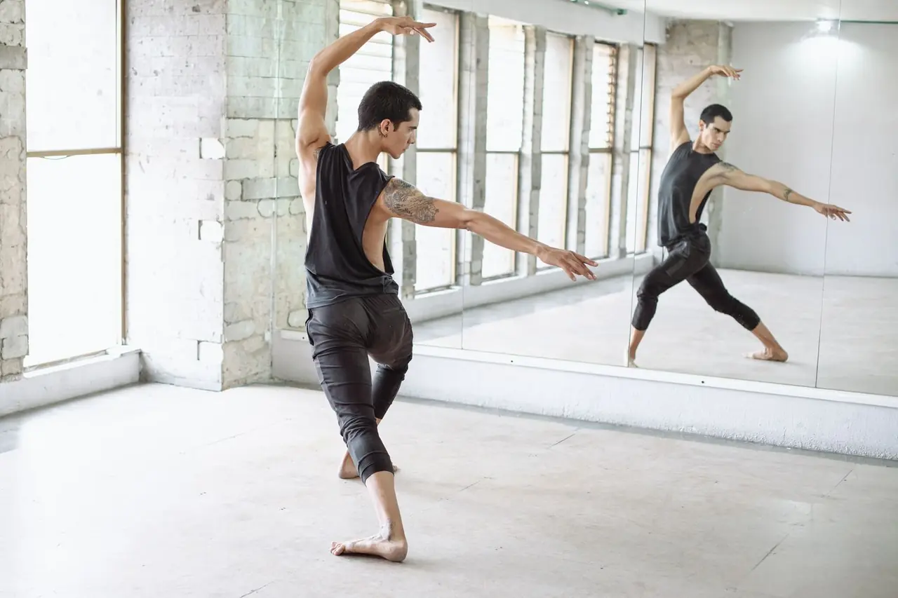 Male ballet dancer studying line and placement before mirrored studio wall